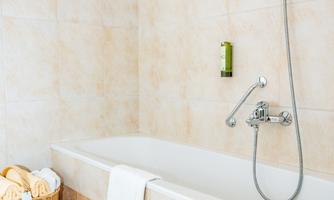 A bright bathroom with a bathtub and a shower head. Next to the bathtub is a laundry basket with towels.