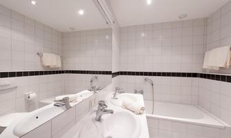 A modern bathroom with white tiles and a bathtub. The amenities include a sink, towels, and a shower.