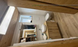 A modern bathroom with wooden shelves and a sink. The floor is wooden and there is plenty of natural light.
