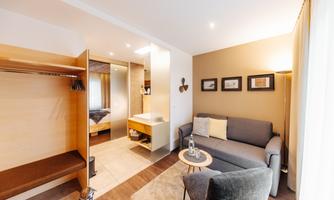 A modern room with a cozy seating area and an open wardrobe. Soft colors and gentle lighting create an inviting atmosphere.