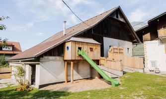 A farmhouse with a play area. A green slide leads from the playhouse to a sizable garden.