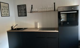 A modern kitchen with a black kitchen unit and a built-in oven. Glasses and a few pictures hang on the wall.