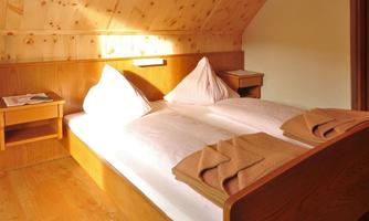 A cozy bedroom with a double bed and wood paneling. Daylight gently pours through the window onto the bright walls and the bed.