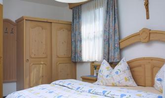 A cozy bedroom with a double bed and wooden wardrobes. The window lets in plenty of daylight and there are decorative curtains.