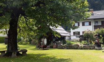 A quiet garden with a large tree and a historic little house. In the background, modern buildings are visible.