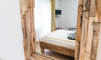 A cozy bedroom with a large bed and light curtains. The frame of the mirror is made of wood and reflects the warm atmosphere of the room.