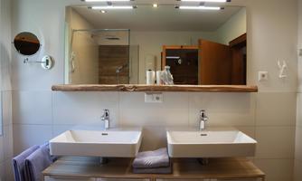 A modern bathroom with two sinks and a large mirror. The walls are painted in light colors, and there are hand towels nearby.