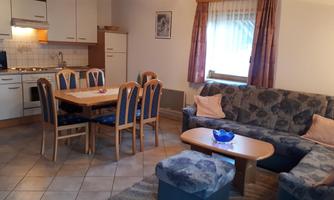 A cozy living kitchen with a dining table, chairs, and a sofa. The kitchenette is modern and well-equipped.