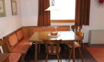 A cozy dining area with a wooden table and padded benches. The windows let in plenty of daylight and create an inviting atmosphere.