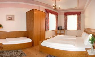 A cozy hotel room with two beds and wooden paneling. The windows let in plenty of daylight, and there is a small table with a television.