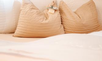 A cozy bed with beige pillows in front of a wooden paneling. The scene radiates tranquility and comfort.