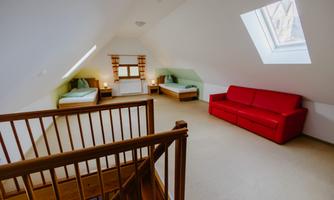 A bright attic room with two single beds and a red sofa. Large windows provide plenty of natural light.