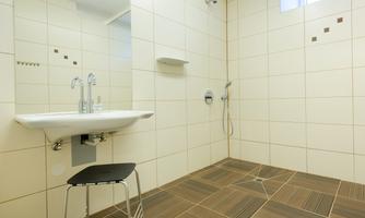 A modern bathroom with a shower and a sink. The walls are tiled in light colors and the floor has brown planks.