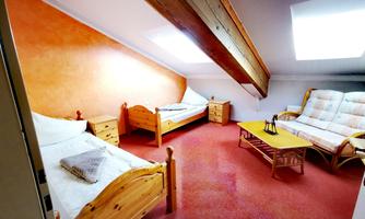 A cozy room with two single beds and a sofa bed. The walls are painted in warm colors, and there is daylight coming through skylights.