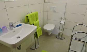 A modern bathroom with white tiles and an elegant decor. Towels in bright green and a laundry rack complete the space.