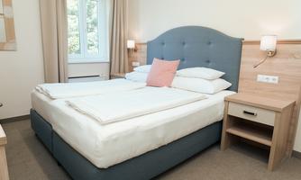 A bright bedroom with a comfortable double bed and modern furniture. There are large windows that let in daylight.