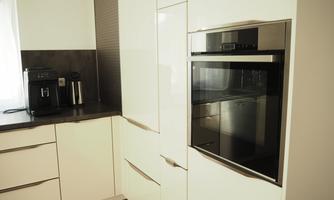A modern kitchen with white cabinets and a wooden countertop. An oven and a coffee machine are visible.
