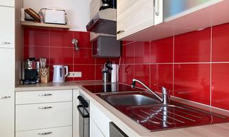 A modern kitchen with red tiles and light cabinets. The equipment includes a stove, a sink, and various kitchen appliances.
