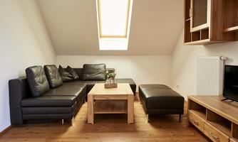 A cozy living room with a black leather couch and a wooden table. A skylight lets in plenty of light.