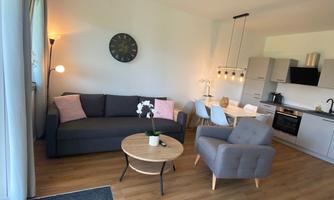 An inviting living room with a gray sofa and a round table. The modern kitchen in the background complements the cozy space.