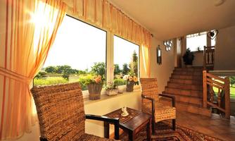 An inviting room with two wicker chairs and a small table. Large windows let in plenty of daylight and offer a view of the green landscape.