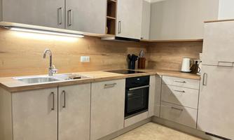 A modern kitchen with light cabinets and wood paneling. It is well-equipped with a stove, a sink, and kitchen appliances.