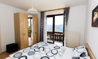 A bright bedroom with a large window and a view of the mountains. The bedding has a modern circular pattern and the room is simply furnished.