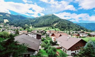 A picturesque mountain landscape with green hills and charming houses. The sky is blue with some white clouds.