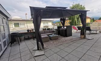 A cozy rooftop terrace with a gazebo, a sofa landscape, and a small table. Surrounded by pots with plants and a beautiful view.