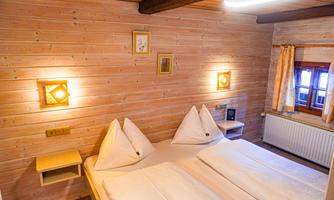 A cozy bedroom with wood paneling and two beds. Soft lighting and windows with curtains create an inviting atmosphere.