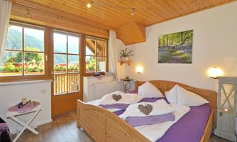 A cozy bedroom with a double bed and wooden ceiling. The room features large windows with a view of the mountains and a lovely balcony.