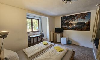 A cozy room with two single beds and a large window. A decorative picture of a landscape hangs on the wall.