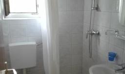 A simple bathroom with shower, sink, and toilet. White tiles and a window ensure brightness.