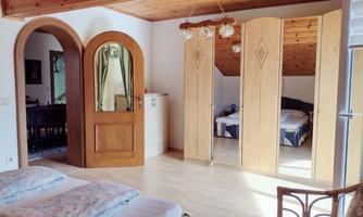 A bright bedroom with wooden ceilings and two beds. In the background, there is a privacy screen and another sleeping area.