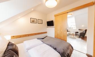 A modern bedroom with a large bed and a wooden sliding door. The room is bright and inviting, with cozy furniture and a television.