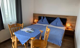 A cozy bedroom with a double bed and blue bedding. A table with two chairs and a small lamp provides illumination, completing the room.