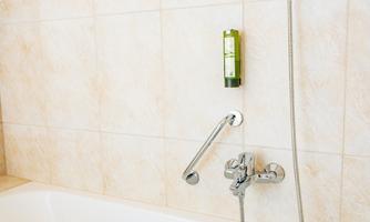 A clean bathtub with a hand shower and a soap dispenser on the wall. The tiles are bright and modern.