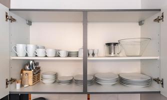 A kitchen cabinet with various dishes. Above are cups and plates, below a bowl and cutlery.