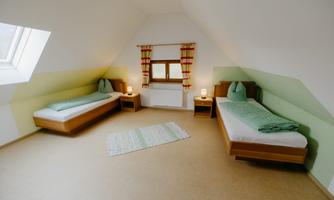 A cozy bedroom with two single beds and a window. The walls are in soft colors, and there is a bright, inviting atmosphere.