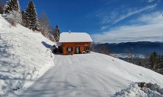 A cozy, orange house in a snowy landscape. The surrounding trees are covered in snow, and the sky is clear and blue.