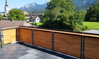 A modern terrace with wooden fences and a view of the mountains. In the background, green meadows and a clear blue sky can be seen.