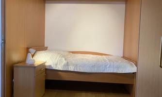 A simple bedroom with a bed and a nightstand. The walls and furniture are in warm wood tones.