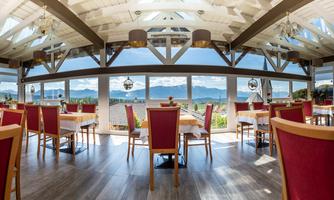 A bright restaurant with large windows and a view of the mountains. The tables are neatly set, and there is an inviting atmosphere in the room.