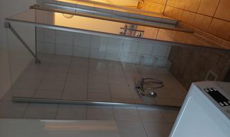 A modern shower with a glass partition in a bright bathroom. In the foreground, a washing machine is visible.