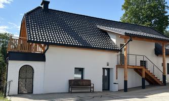 A modern house with a dark roof and wooden cladding. The facade is light and there is a terrace as well as an entrance with a staircase.