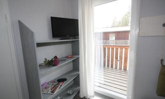 A cozy room with a television and an open balcony. Bright curtains let in plenty of daylight.