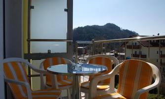 A balcony with four chairs and a table. In the background, hills and a blue sky can be seen.
