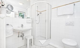 A modern bathroom with a shower, a sink, and a toilet. The walls are tiled in white, and the décor is bright and welcoming.