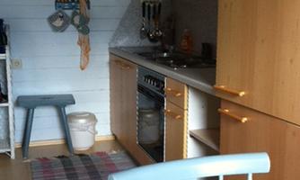 A small kitchen with wooden cabinets and a modern cooking facility. On the floor lies a striped rug, and a clock is hanging on the wall.