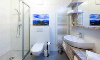 A modern bathroom with a shower, toilet, and sink. The wall is light-colored, and there are decorative pictures.